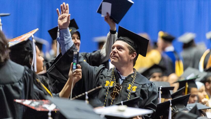 A man looks up and raises his hand at commencement