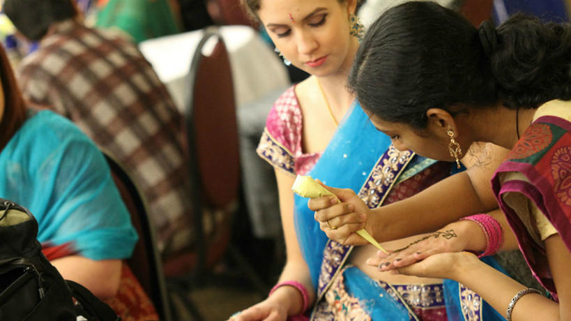Student applying henna on another student during Global Fest