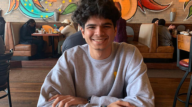 A photo of UM-Dearborn graduate student Rudra Mehta sitting at a table at a coffee shop in downtown Dearborn.